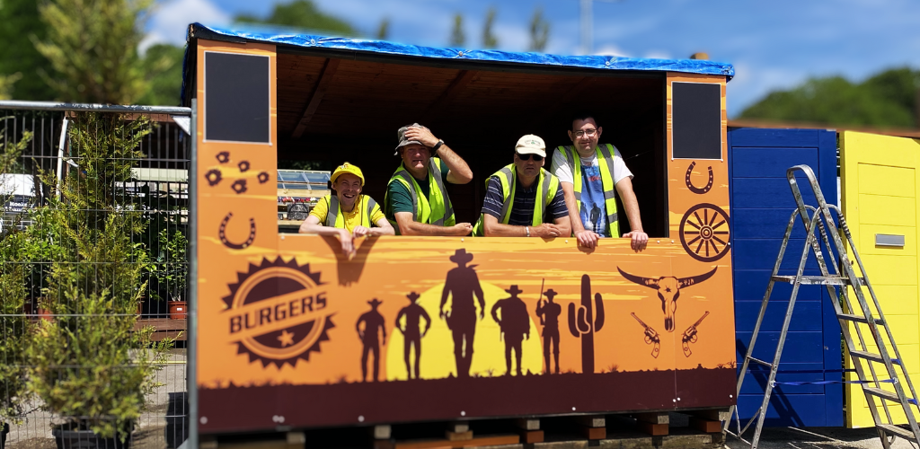 A group of students in hi-vis jackets standing in a newly-built hut for our Artisan Markets. The boys are giving thumbs up and smiling.