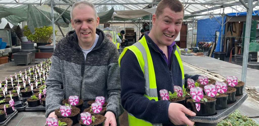 Two students holding a tray of petunias that have been freshly planted ahead of the Summer Season.